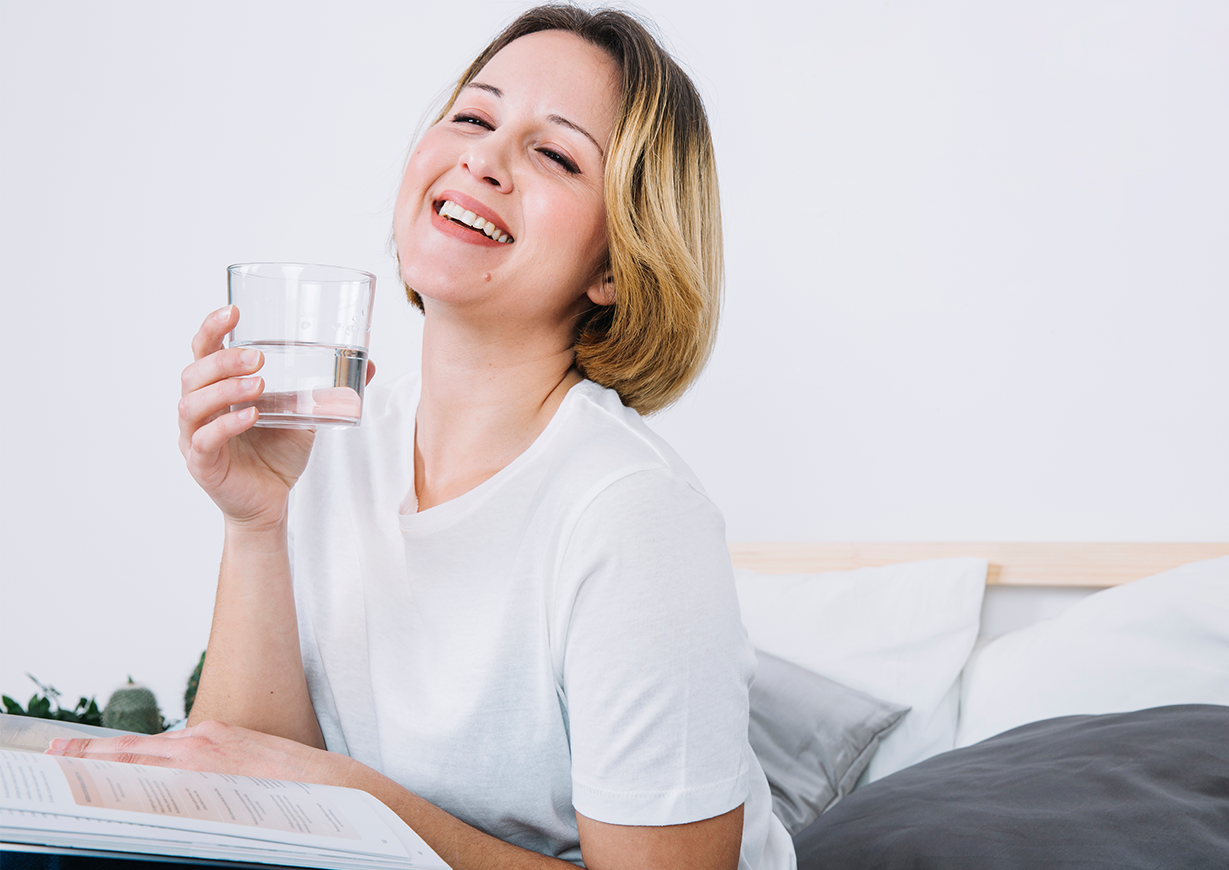 A cheerful woman smiling brightly as she holds a glass of water, reflecting the joy of fresh, healthy living with Fil-Fresh water filters