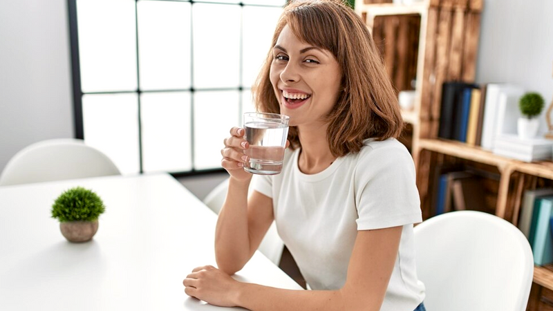 Young woman smiling brightly while holding a refreshing glass of water filtered through Fil-Fresh replacement filter