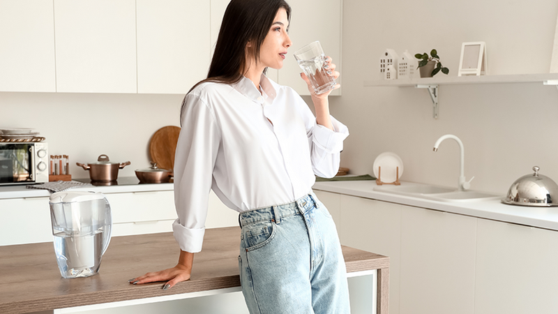 Young woman drinking water filtered with a Fil-Fresh pitcher filter by the kitchen counter