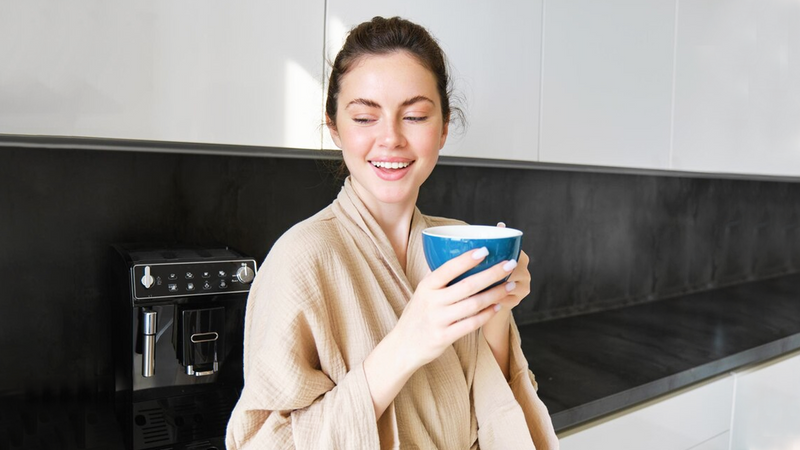 Woman relaxing with a fresh cup of coffee made using filtered water by the kitchen coffee machine