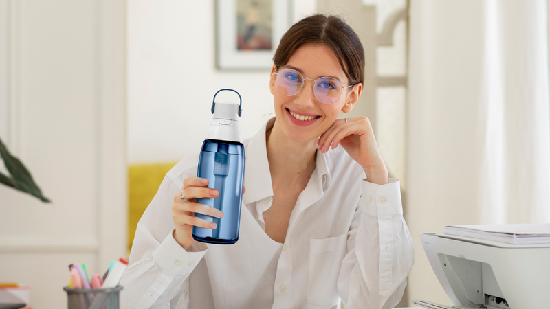 Smiling woman at her office desk holding a water bottle filtered with Fil-Fresh replacement filter