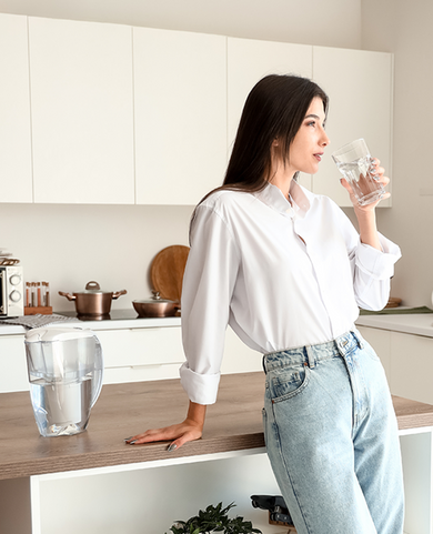 Young woman drinking water filtered with a Fil-Fresh pitcher filter by the kitchen counter