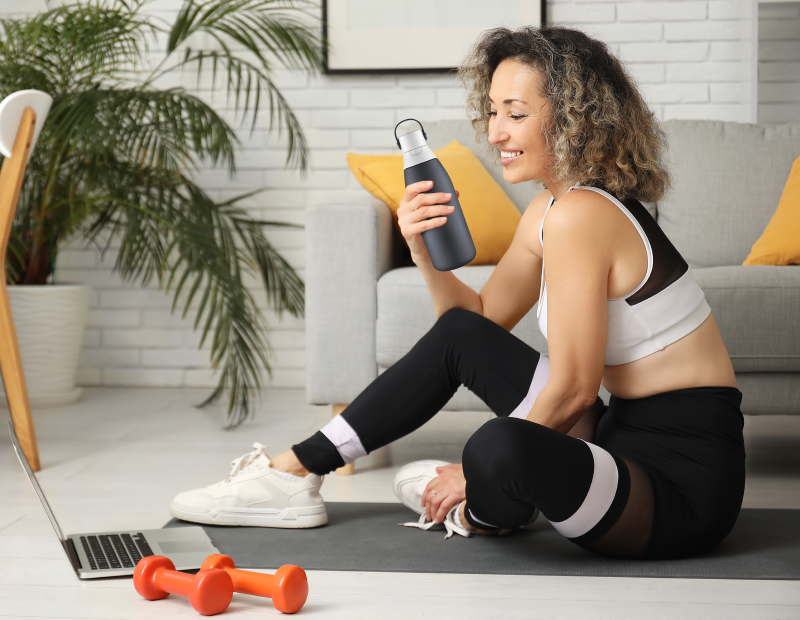 Young woman sitting on a yoga mat indoors holding a water bottle featuring a Fil-Fresh water bottle filter