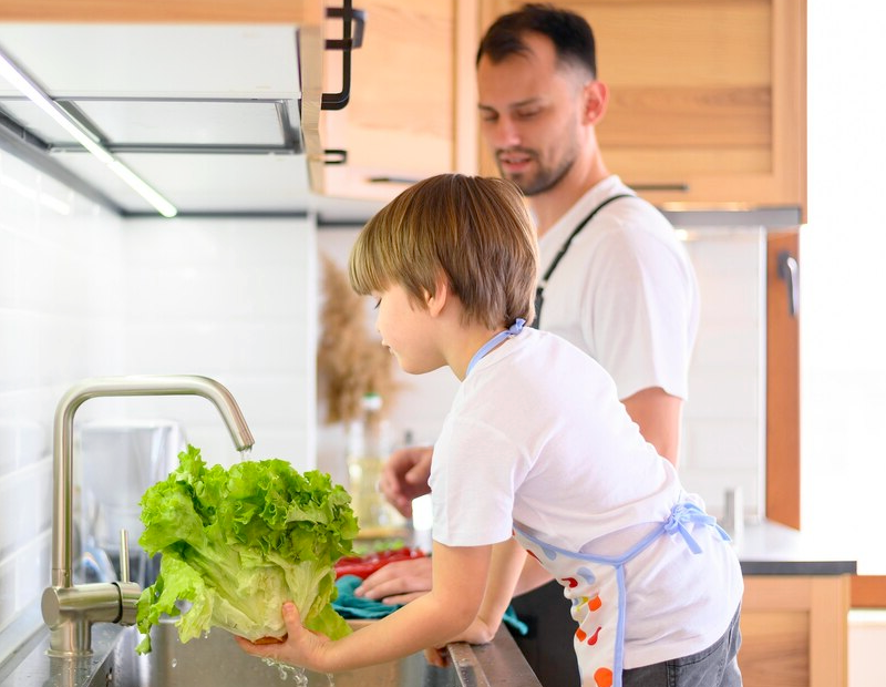 Father and son washing fresh vegetables at the kitchen sink using clean water filtered through a Fil-Fresh faucet filter replacement